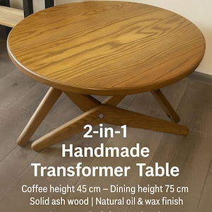 May include: A round, light brown wooden transformer table. The table has a coffee height of 45 cm and a dining height of 75 cm. The table is made of solid ash wood with a natural oil and wax finish. The text on the table says "2-in-1 Handmade Transformer Table."