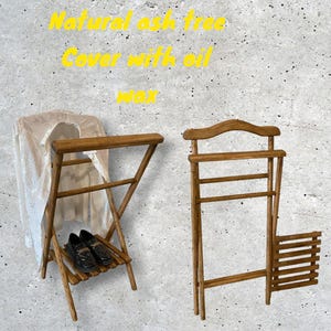 Könnte beinhalten: Zwei Holz-Kleiderständer mit natürlicher Asche-Oberfläche. Der Ständer links hat ein Regal für Schuhe und ein weißes Kleidungsstück hängt daran. Der Ständer rechts hat ein Regal zum Aufhängen von Kleidung. Beide Ständer sind faltbar.
