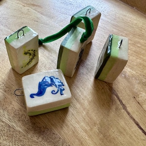Peut inclure: Ornements en c&eacute;ramique faits &agrave; la main de forme carr&eacute;e et rectangulaire. Les ornements sont blanc cass&eacute; avec des accents verts et bleus. L'un a un motif bleu, et un autre un ruban de velours vert.
