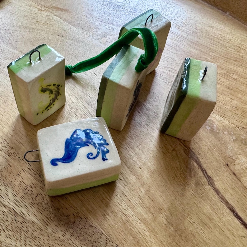 Peut inclure: Ornements en c&eacute;ramique faits &agrave; la main de forme carr&eacute;e et rectangulaire. Les ornements sont blanc cass&eacute; avec des accents verts et bleus. L'un a un motif bleu, et un autre un ruban de velours vert.
