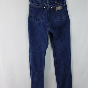 May include: A pair of dark blue denim jeans with a brown leather patch on the back pocket that says "Wrangler".