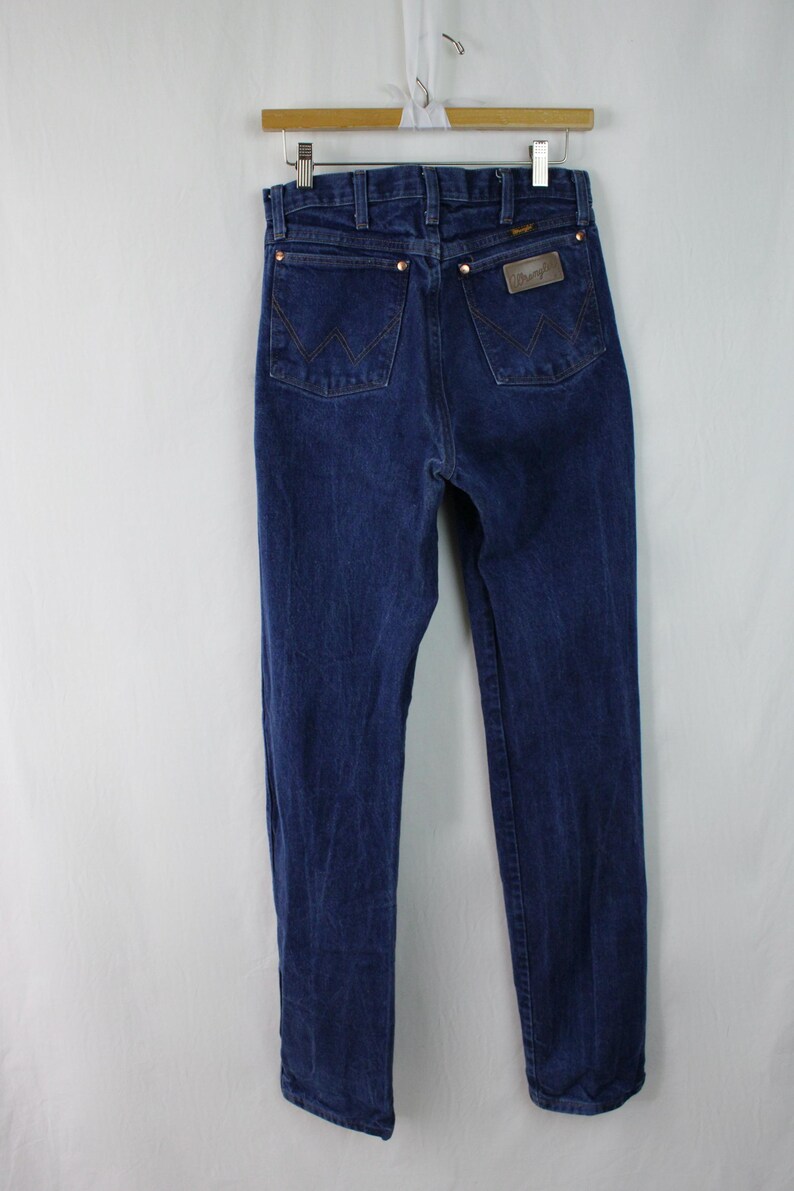 May include: A pair of dark blue denim jeans with a brown leather patch on the back pocket that says "Wrangler".
