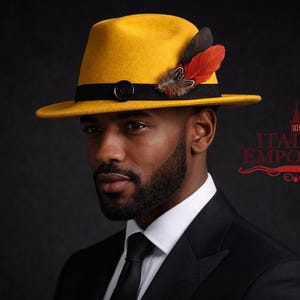 Puede incluir: Un sombrero fedora amarillo mostaza con una banda negra y plumas decorativas. El sombrero se usa con un traje y corbata negros. La imagen está sobre un fondo oscuro.