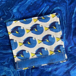 May include: A white fabric pocket with a blue and yellow fish pattern. The pocket has a blue velcro strap.