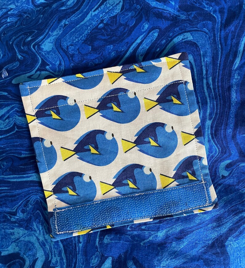 May include: A white fabric pocket with a blue and yellow fish pattern. The pocket has a blue velcro strap.