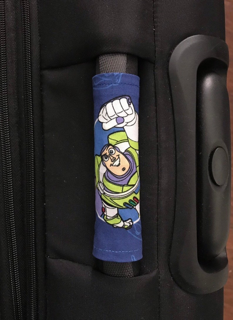 May include: A blue luggage handle cover with a cartoon image of Buzz Lightyear from the Toy Story movie franchise. The cover is made of fabric and has a white zipper.