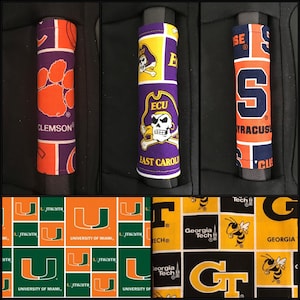 Op de afbeelding: Een set van zes autostoel handgreephoezen met verschillende college logo's. De logo's omvatten Clemson, East Carolina, Syracuse, Miami, Georgia Tech en Georgia. De hoezen zijn gemaakt van stof en hebben een patchwork ontwerp.