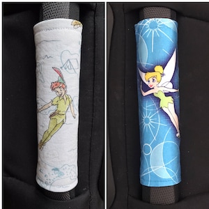 May include: Two car seat belt covers, one with a blue background and a Tinkerbell illustration, the other with a white background and a Peter Pan illustration.