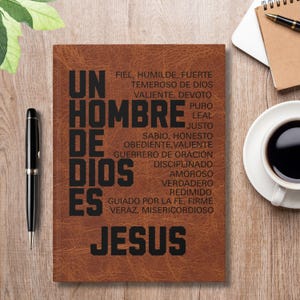 Op de afbeelding: Een bruin leren notitieboek met de tekst "UN HOMBRE DE DIOS ES JESUS" in het zwart. Extra tekst geeft eigenschappen als "trouw" en "nederig" weer. Een pen en een kopje koffie zijn zichtbaar.