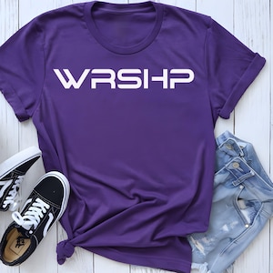 Puede incluir: Camiseta morada con la palabra "WRSHP" impresa en blanco en la parte delantera.