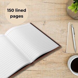An open hardcover journal with 150 lined pages rests on a light wood desk, the clean white pages fanned open to show dark evenly spaced horizontal lines. To the right sits a silver pen on top of a kraft notebook, beside a steaming cup of black coffee in a white mug. A small green succulent in a glass pot adds a touch of nature. At the top left, a beige circle graphic displays the words “150 lined pages” in bold black text.