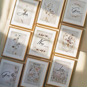 Puede incluir: Una colección de grabados artísticos enmarcados con marcos dorados. Cada grabado presenta ilustraciones florales y textos inspiradores como "Abide in me", "Grow in grace" y "Love". La obra de arte tiene una paleta de colores neutros con tonos beige, marrón y blanco.