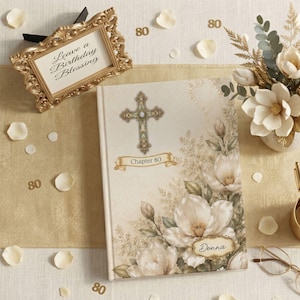 Puede incluir: Un libro de tapa dura con cubierta color crema que presenta una cruz decorativa, ilustraciones florales y el texto Chapter 80 y Donna. El libro se muestra con un marco dorado que contiene el texto Leave a Birthday Blessing.