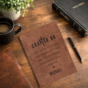 Puede incluir: Un cuaderno marrón texturizado con el texto impreso en negro CHAPTER 80, Eight decades of blessings, A life shaped by God's hand, Years filled with wisdom, A legacy built to endure, Psalm 71:18, y el nombre MICHAEL, con un símbolo de cruz.