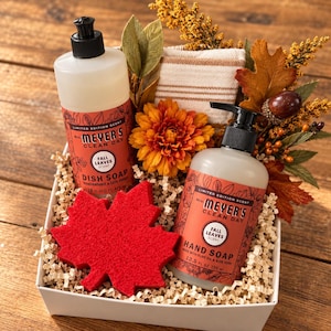May include: A gift set containing a 16 fl oz bottle of Mrs. Meyer's Clean Day Fall Leaves dish soap, a 12.5 fl oz bottle of hand soap, a red maple leaf-shaped sponge, a striped cloth, and decorative autumn foliage in a white box.