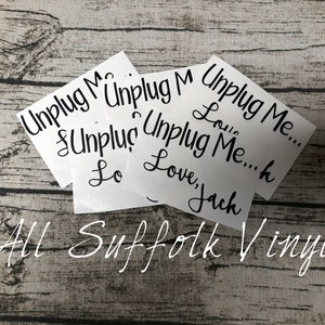 May include: Four white vinyl stickers with the text "Unplug Me..." in black cursive writing. The stickers are stacked on top of each other. The text "Love, Jack" and "Lou" are visible on the bottom sticker. The text "All Suffolk Vinyl" is written in white cursive on a wooden background.