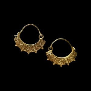 Puede incluir: Un par de pendientes de aro de oro con un patrón geométrico. Los pendientes son pequeños y delicados.