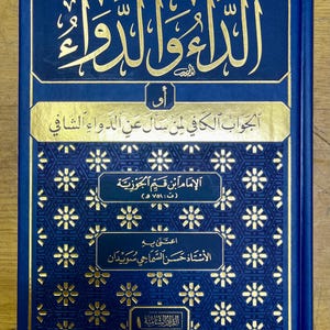 May include: A hardback book with a dark blue cover and gold lettering. The title is in Arabic script, with additional gold text. The book has a decorative floral pattern and is likely a religious text.