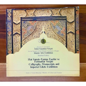 May include: A poster for an Islamic Arts Exhibition in Istanbul, Turkey. The poster features a decorative border with intricate patterns in gold and blue. The text on the poster reads "Hicret'in 15. Yüzyılda İslâm Sanatları Sergisi" and "On the Occasion of the Fifteenth Centennial of Hegira Islamic Arts Exhibition Istanbul-Turkey".