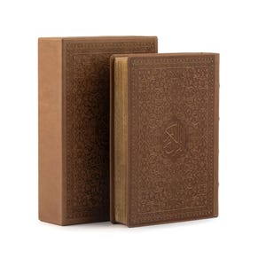 May include: Two brown leather-bound books with intricate embossed designs. The larger book has the word "القرآن" in Arabic script on the cover.