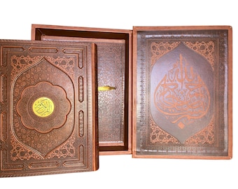 May include: A brown, ornately decorated book with gold accents, open inside a matching box. The cover features intricate patterns and a central medallion. The open pages display Arabic calligraphy in a copper color.