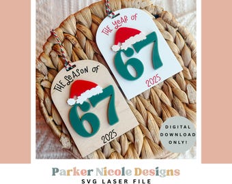 May include: Two Christmas ornaments with the text "The Season of 67 2025" and "The Year of 67 2025". Each ornament has a red Santa hat and green numbers. The ornaments are on a woven basket.