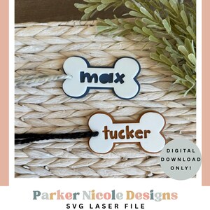 May include: Two bone-shaped pet tags, one navy blue and white, the other brown and white. The navy tag says "max" and the brown tag says "tucker". Both tags are on a woven background. The tags are for pets.