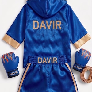May include: A blue satin boxing robe with a hood and gold trim, featuring the text DAVIR in gold on the back. Matching blue satin shorts with gold side stripes and the text DAVIR on the waistband. Two blue boxing gloves with flame graphics.