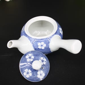 May include: A white and blue ceramic teapot with a lid. The teapot has a round body with a handle and a spout. The lid is decorated with white floral patterns. The teapot is designed for tea service.