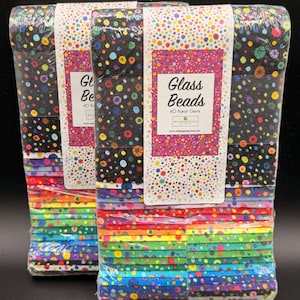 May include: Two stacks of fabric squares wrapped in clear plastic. The top fabric features a black background with multicolored polka dots. A white paper label on the front reads Glass Beads 40 Karat Gems Wilmington Prints. The lower fabric layers show a rainbow of solid colors and patterned strips.