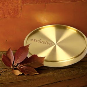 May include: A gold-colored round coaster with a shiny, reflective surface. The coaster has the word "exclusive" engraved on it.