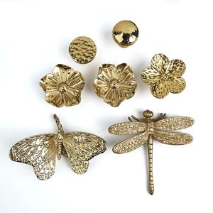 May include: A set of gold-toned metal drawer pulls featuring a variety of nature-inspired designs, including butterflies, dragonflies, and flowers.