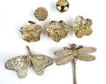 Puede incluir: Un juego de tiradores de cajones de metal dorado con una variedad de diseños inspirados en la naturaleza, incluyendo mariposas, libélulas y flores.