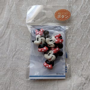 May include: A package of Minnie Mouse-shaped buttons. The buttons are white, black, and red, with Minnie's signature bow and dress. The package has Japanese text and the Disney logo.