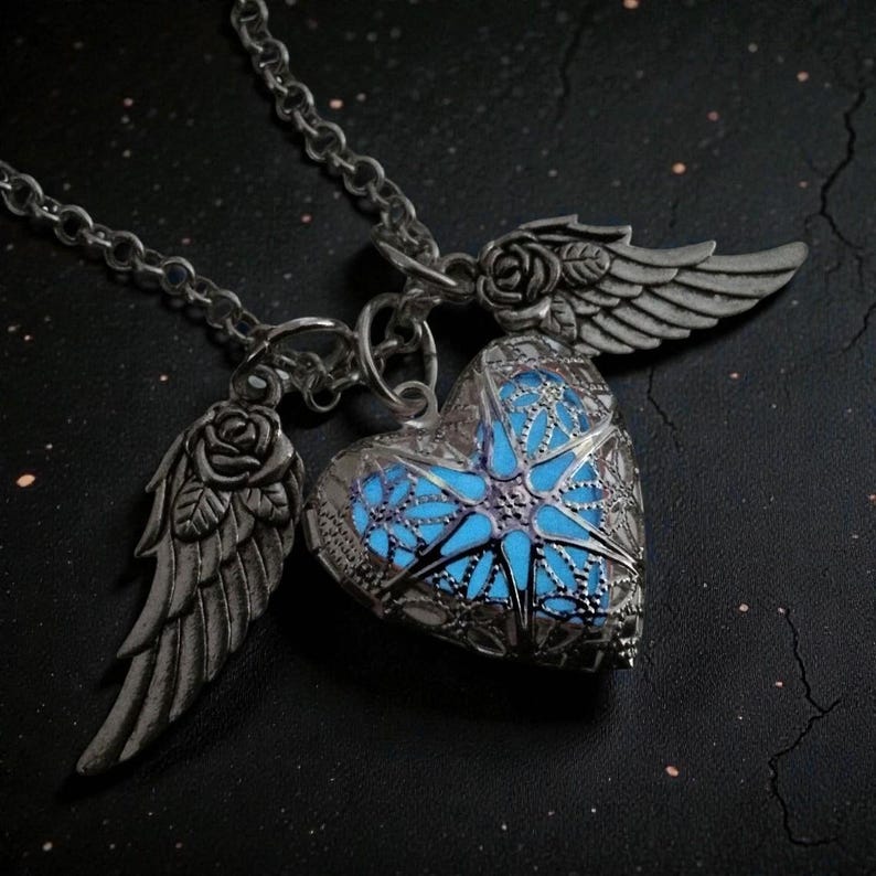 Pu&ograve; includere: Collana color argento con ciondolo a forma di cuore con interno blu brillante e design traforato. Il ciondolo &egrave; affiancato da due ali con dettagli di rose. La catena della collana &egrave; visibile.