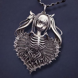 May include: Silver-toned pendant necklace featuring a stylized anime-style girl with pigtails and a skeleton torso. The pendant has a heart-shaped design with intricate details and a chain. The necklace is displayed against a dark background.