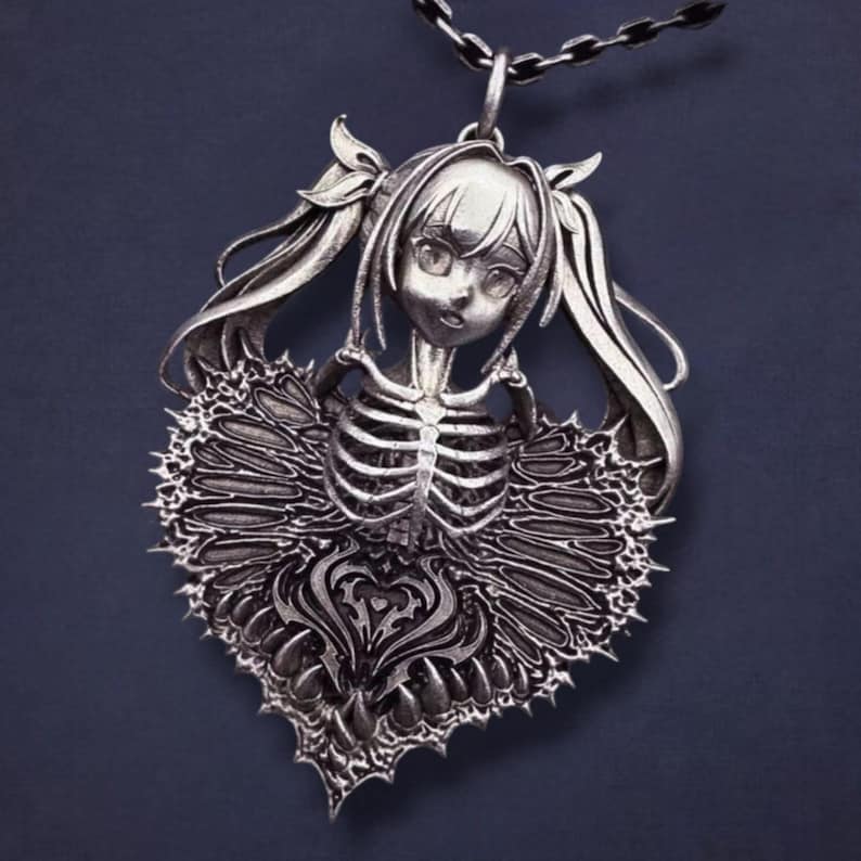 May include: Silver-toned pendant necklace featuring a stylized anime-style girl with pigtails and a skeleton torso. The pendant has a heart-shaped design with intricate details and a chain. The necklace is displayed against a dark background.