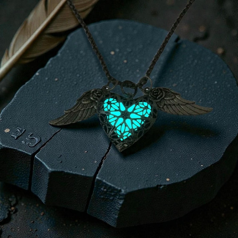 Pu&ograve; includere: Una collana con pendente a forma di cuore color bronzo con ali e un centro turchese luminoso. Il pendente &egrave; su un cordino scuro e poggia su una superficie scura e strutturata. Le ali sono dettagliate e il cuore ha un design a filigrana.
