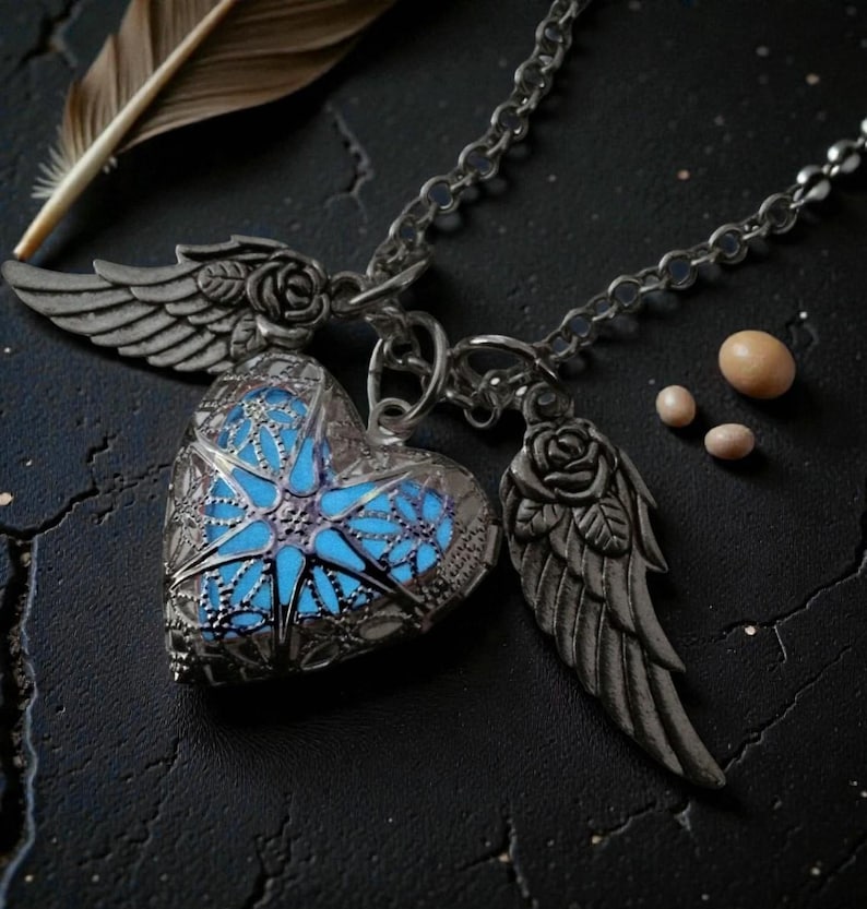 Pu&ograve; includere: Una collana con pendente a forma di cuore argentato con un centro blu brillante, ali e accenti di rose. La collana &egrave; su una catena ed &egrave; accompagnata da una piuma e piccole perle rotonde. Il ciondolo ha un design intricato e traforato.
