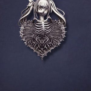 May include: A silver-colored pendant featuring a stylized anime girl design. The pendant has a skeleton-themed bodice and a heart-shaped lower section with intricate detailing. The girl has long pigtails and a delicate facial expression.