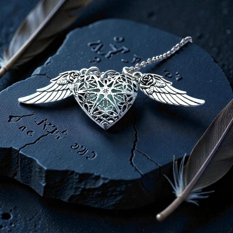 Pu&ograve; includere: Una collana con pendente a forma di cuore color argento con design traforato, ali e catena. Il cuore ha un centro verde ed &egrave; adornato da piccole rose. La collana poggia su una superficie blu scuro strutturata con piume.