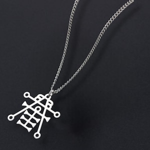 May include: Silver-colored pendant necklace featuring a geometric design. The pendant is suspended from a delicate chain. The necklace is displayed against a dark background, highlighting the intricate details of the pendant.