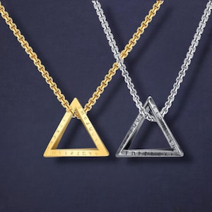 May include: Two triangle pendant necklaces. One is gold-toned, the other silver-toned, each suspended from a matching chain. The pendants feature engraved text around the edges. The background is a dark blue.