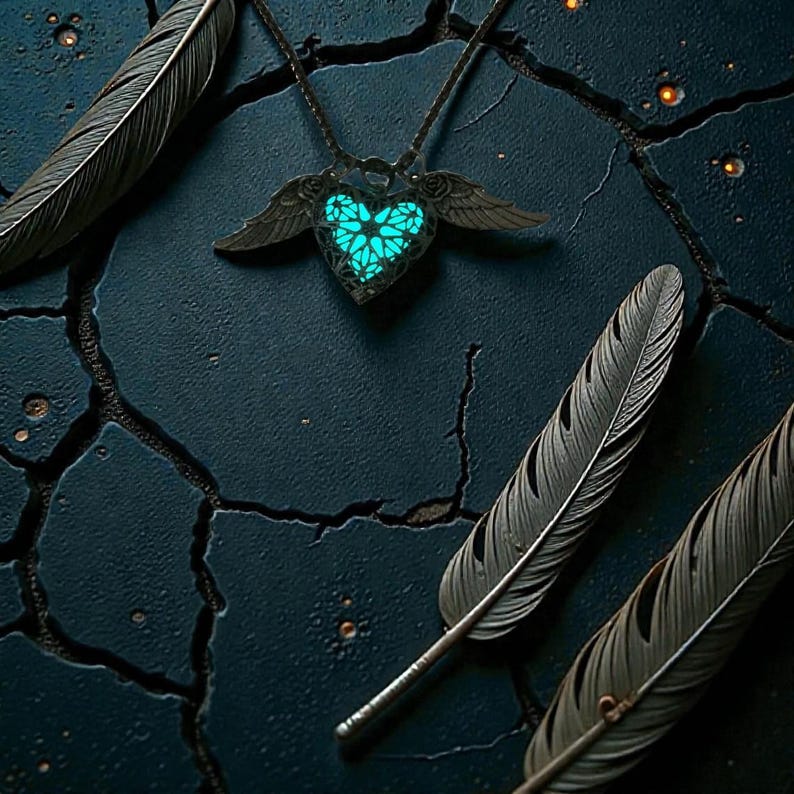 Pu&ograve; includere: Una collana con un ciondolo a forma di cuore turchese brillante, incorniciato da ali, poggia su una superficie scura e strutturata. Tre piume scure sono disposte attorno alla collana. Il cuore del ciondolo &egrave; decorato con un design intricato.