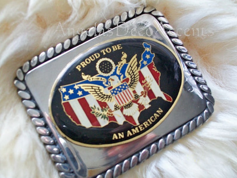 May include: Silver belt buckle with a black and gold oval design. The oval features a map of the United States with an eagle and the words "Proud to be an American".