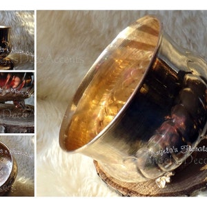 May include: A metallic gold decorative bowl with a wide opening, set on a wooden slice. The bowl features a detailed, textured design and is supported by ornate feet. The image includes the text "Angela's Florals & More".