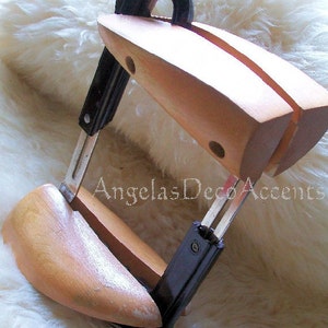 K&ouml;nnte beinhalten: Ein Schuhspanner aus Holz mit schwarzem Griff und Metallkomponenten. Der Schuhspanner ist hellbraun und hat eine gebogene Form, um in einen Schuh zu passen. Der Text "Angelas Deco Accents" ist sichtbar.