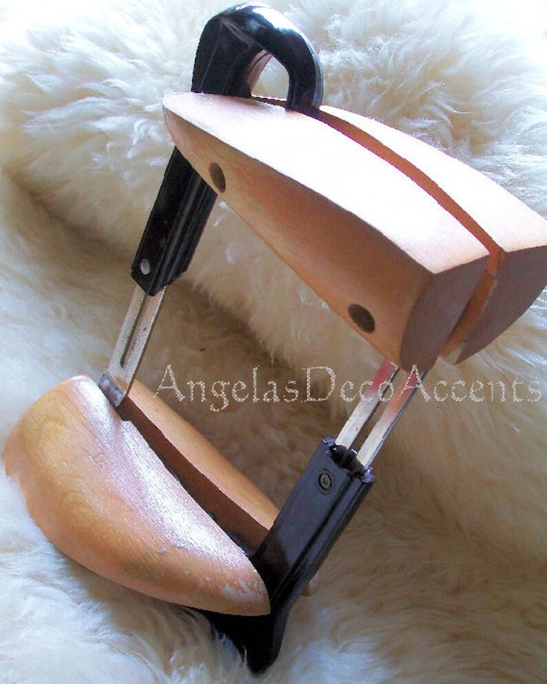 K&ouml;nnte beinhalten: Ein Schuhspanner aus Holz mit schwarzem Griff und Metallkomponenten. Der Schuhspanner ist hellbraun und hat eine gebogene Form, um in einen Schuh zu passen. Der Text "Angelas Deco Accents" ist sichtbar.