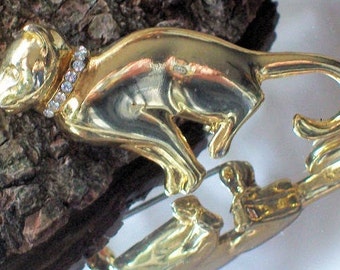 May include: A gold-coloured metal brooch depicting a running cat. The cat has a collar adorned with clear rhinestones. The brooch is highly reflective and appears vintage. This is a jewellery item.