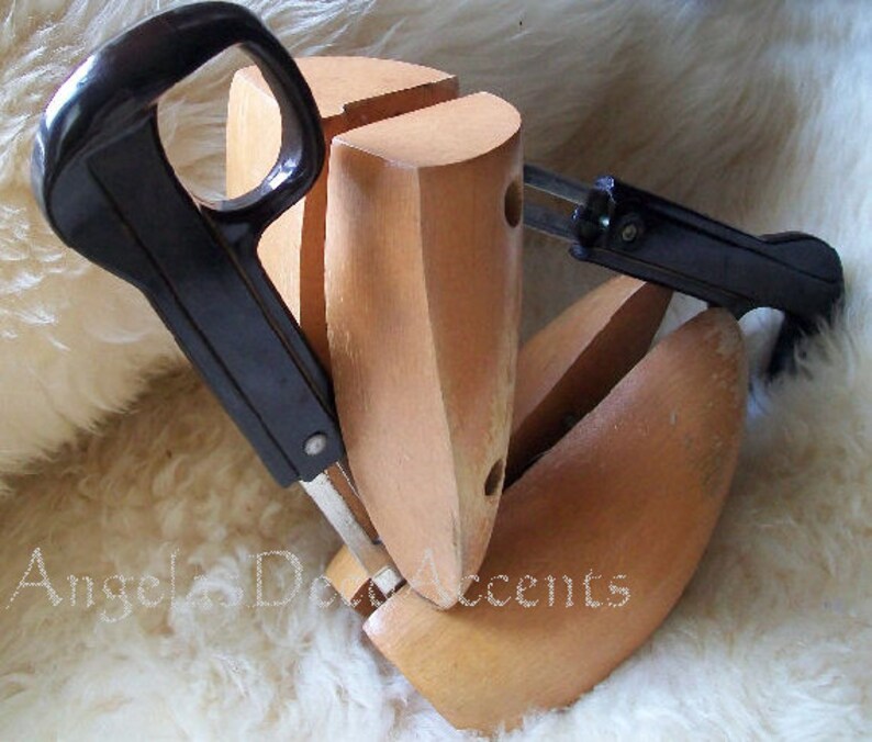 K&ouml;nnte beinhalten: Schuhspanner aus Holz mit schwarzen Griffen und Metallkomponenten. Die Schuhspanner sind hellbraun und sollen die Form der Schuhe erhalten. Das Bild ist vor einem wei&szlig;en, flauschigen Hintergrund aufgenommen.